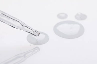 Photo of Glass pipette and transparent liquid on white background, closeup