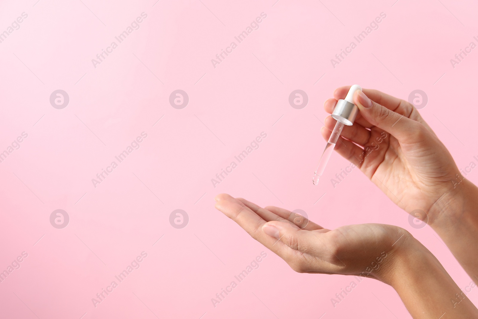 Photo of Woman applying cosmetic serum onto her hand on pink background, closeup. Space for text