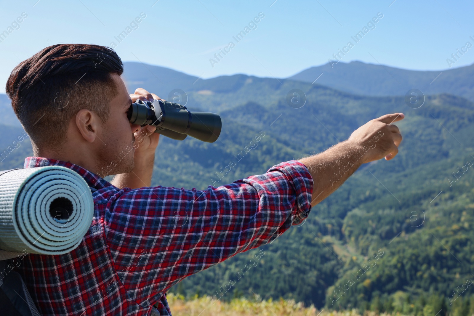 Photo of Tourist with hiking equipment looking through binoculars in mountains