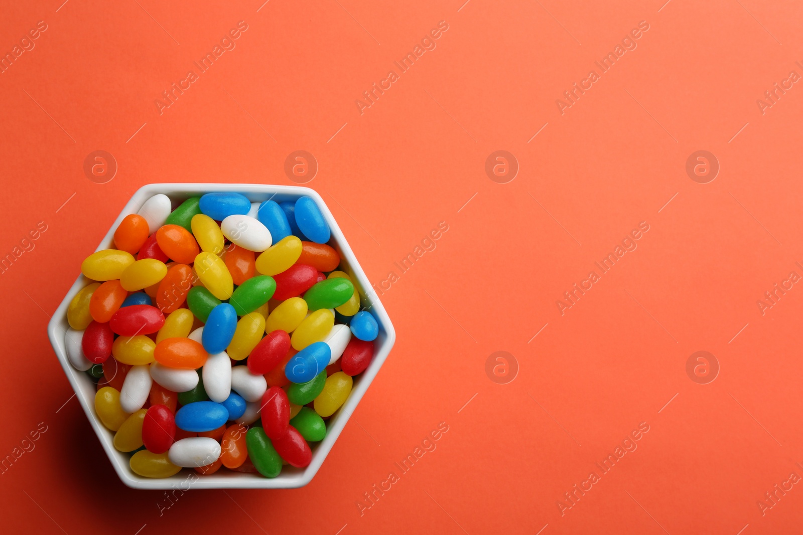 Photo of Bowl with colorful jelly beans on coral background, top view. Space for text