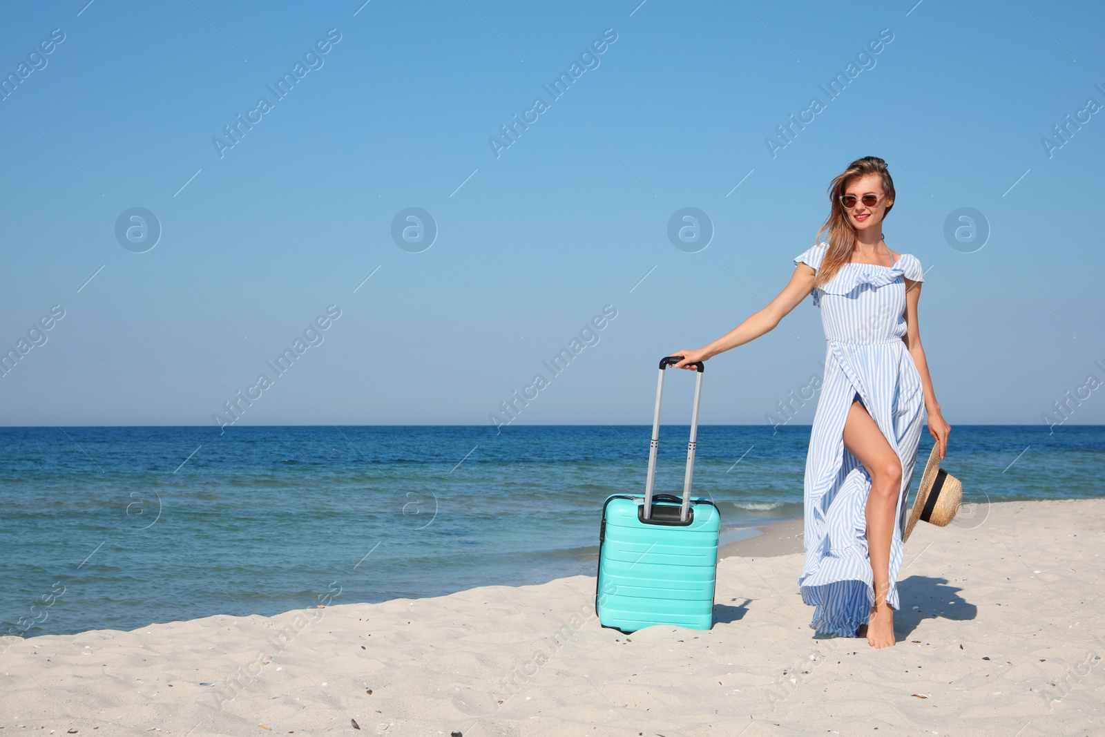 Photo of Beautiful woman with suitcase on sandy beach near sea