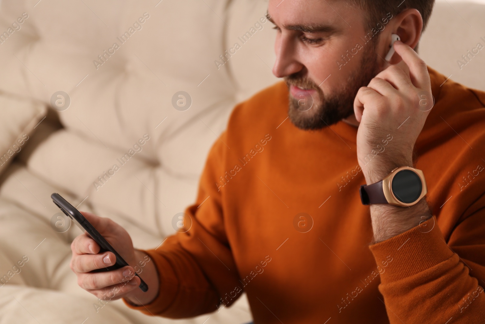 Photo of Young man with smart watch, phone and earphones at home
