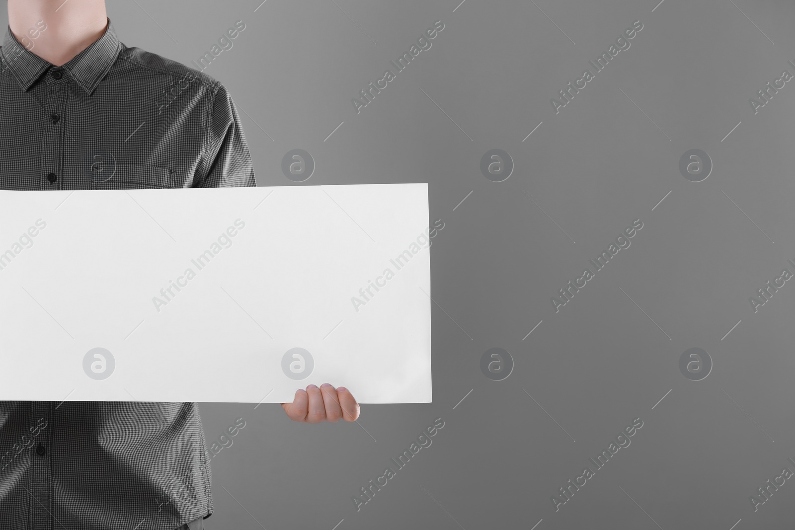 Photo of Man holding sheet of paper on grey background, closeup. Mockup for design