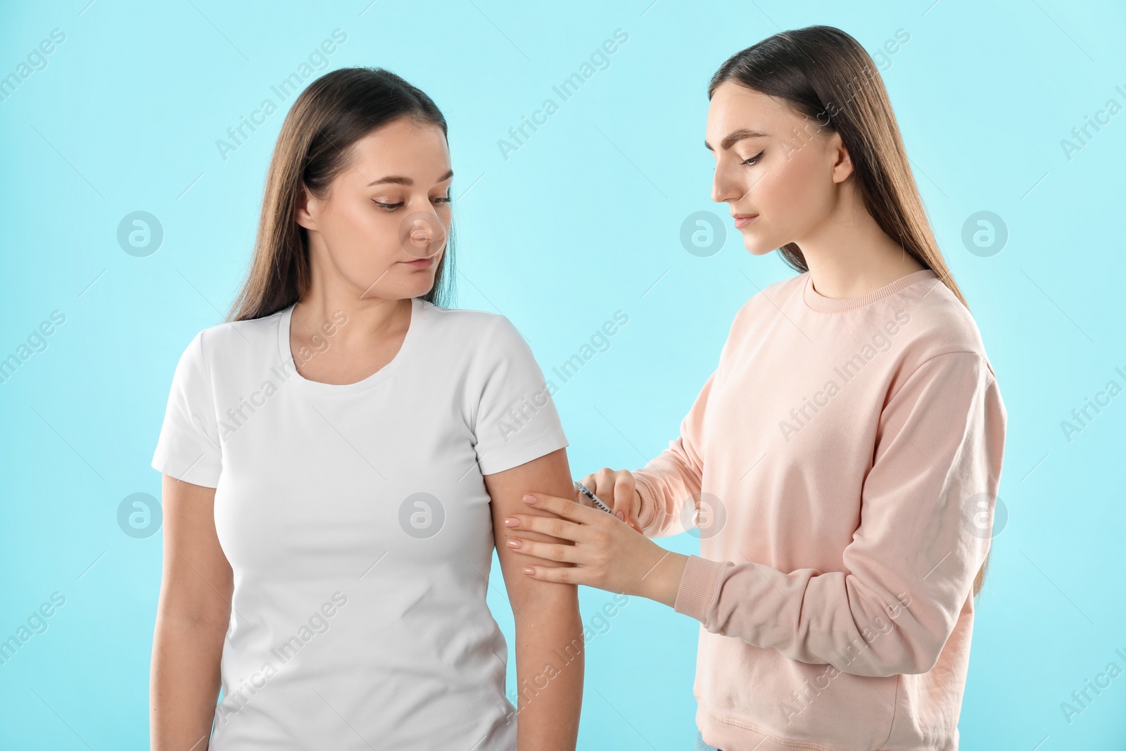 Photo of Woman giving insulin injection to her diabetic friend on light blue background