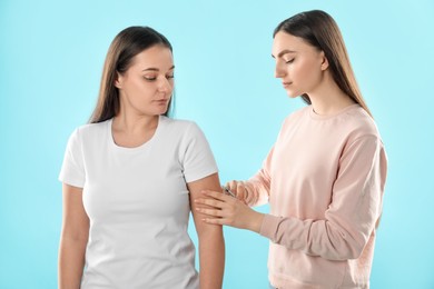Woman giving insulin injection to her diabetic friend on light blue background