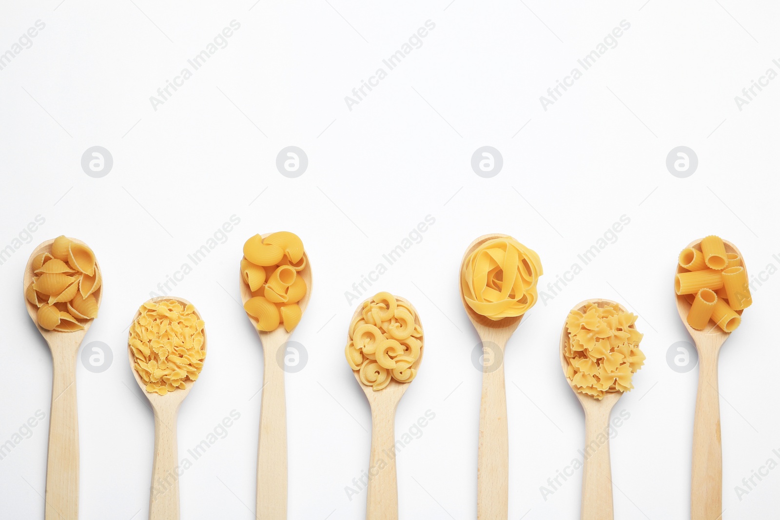 Photo of Different types of pasta in spoons on white background, flat lay. Space for text