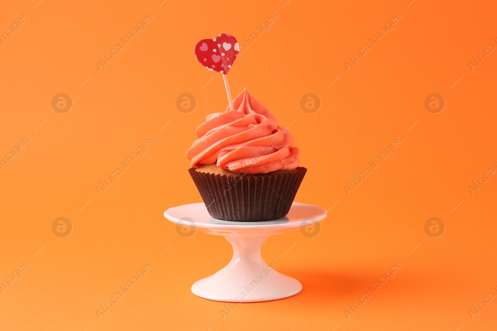 Photo of Delicious cupcake with bright cream and heart topper on orange background