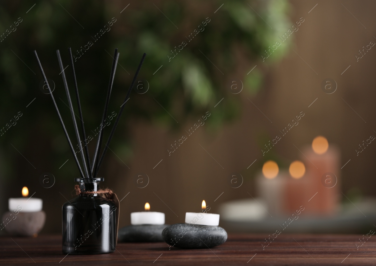 Photo of Reed air freshener, spa stones and burning candles on wooden table. Space for text