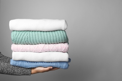 Photo of Woman holding stack of warm clothes on grey background, closeup. Autumn season