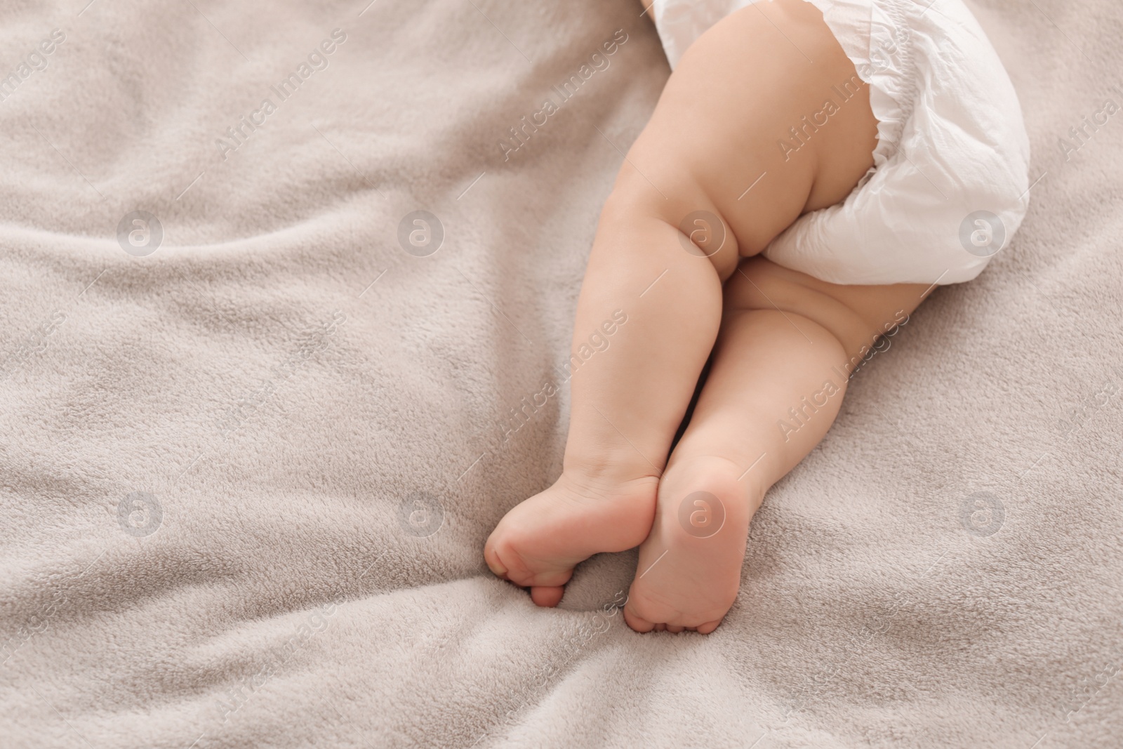 Photo of Cute little baby lying on bed, closeup of legs. Space for text