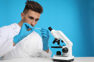 Photo of Man with slide and microscope at white table on blue background. Medical research