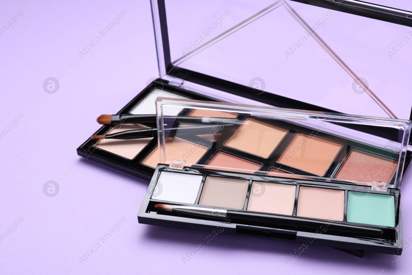 Photo of Colorful contouring palettes with brushes on violet background, closeup. Professional cosmetic product