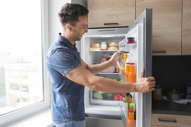 Man taking bottle with water out of refrigerator in kitchen