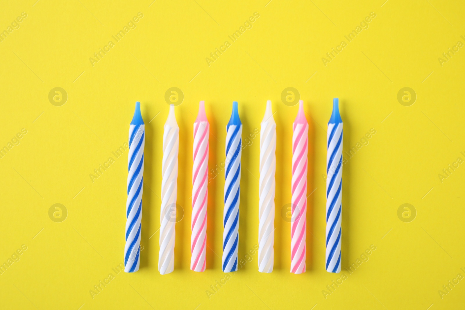Photo of Colorful striped birthday candles on yellow background, flat lay
