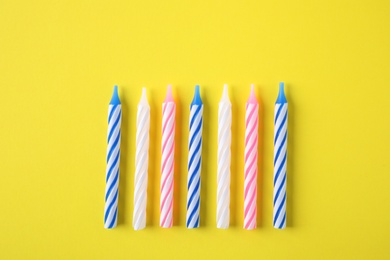 Colorful striped birthday candles on yellow background, flat lay