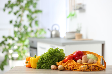 Net bags with vegetables on wooden table in kitchen