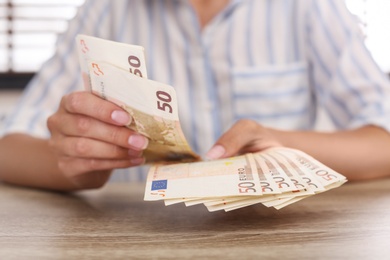 Photo of Woman with Euro banknotes at wooden table indoors, closeup