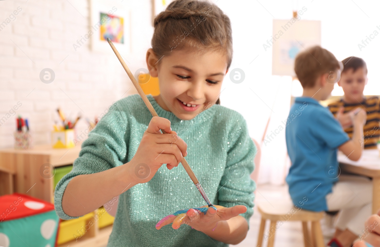 Photo of Cute little child painting her palm at table in room