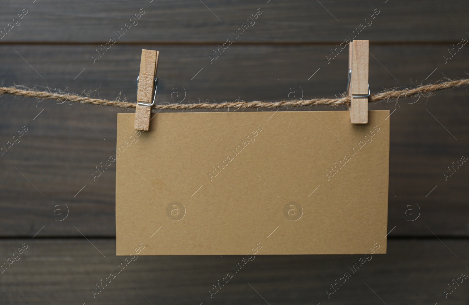 Photo of Clothespins with blank notepaper on twine against wooden background. Space for text