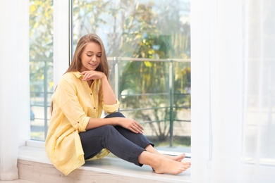 Photo of Young woman sitting near window with open curtains at home