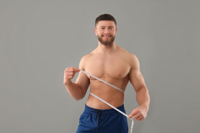 Photo of Happy athletic man measuring waist with tape on grey background. Weight loss concept