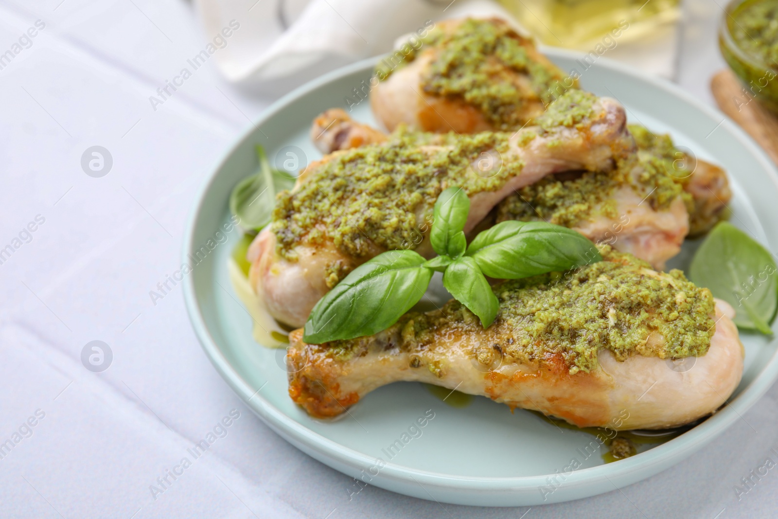 Photo of Delicious fried chicken drumsticks with pesto sauce and basil on white table, closeup. Space for text