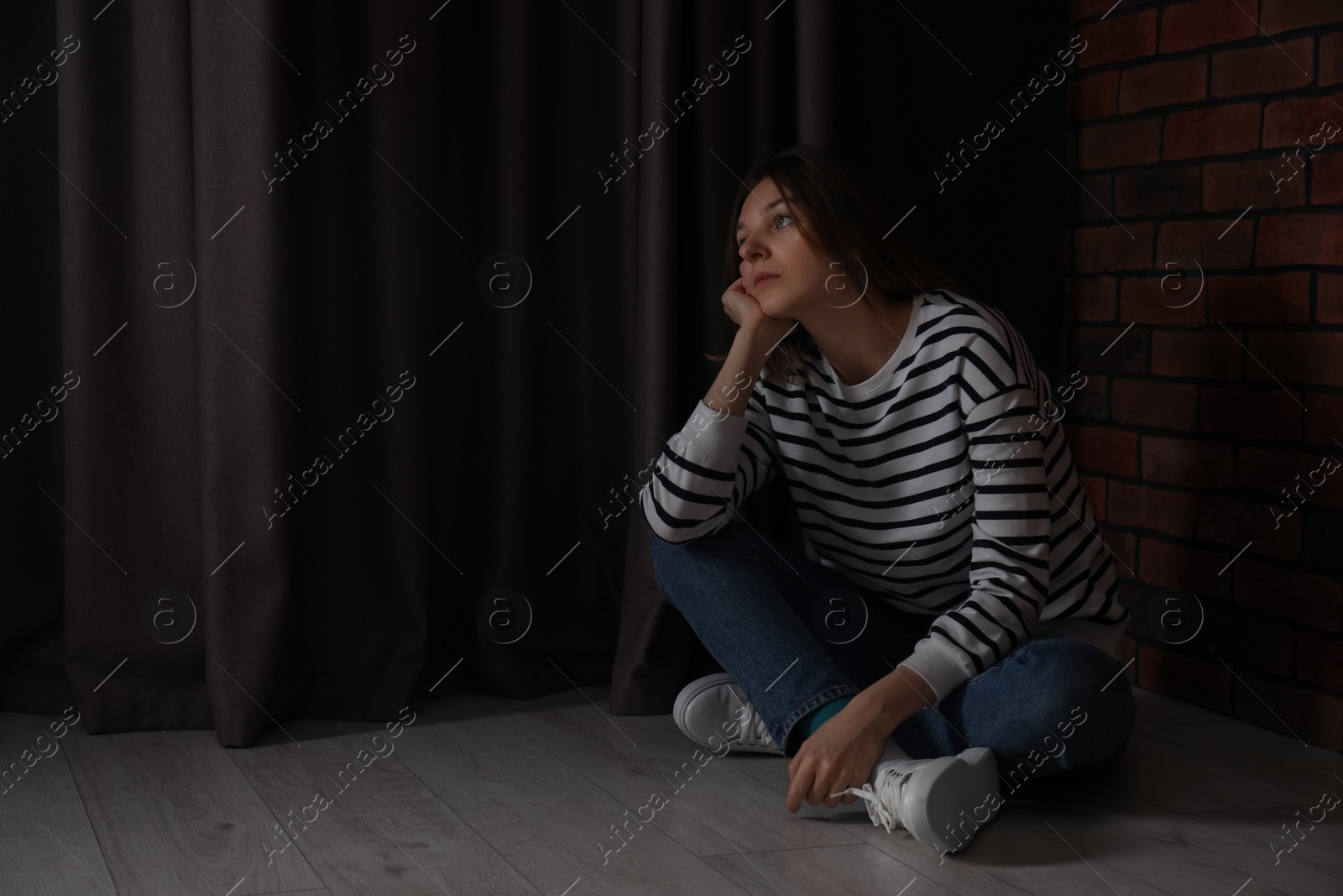 Photo of Sad young woman sitting on floor indoors, space for text