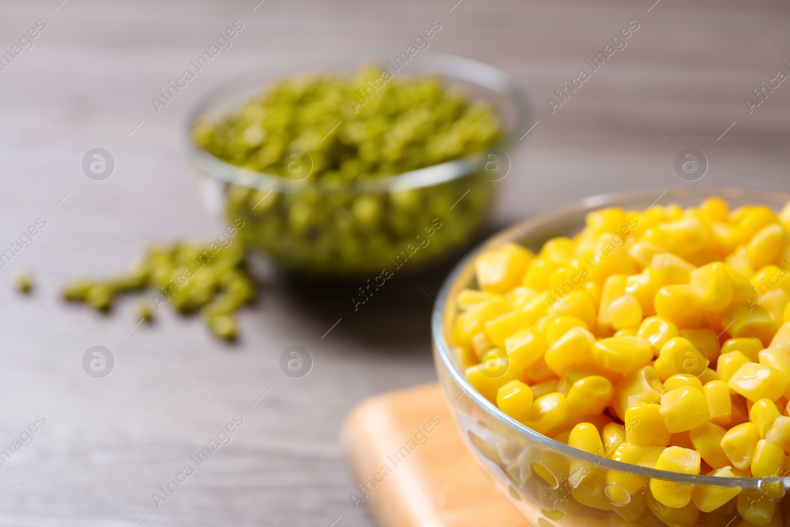 Photo of Glass bowl of canned sweet corn on wooden table, closeup. Space for text