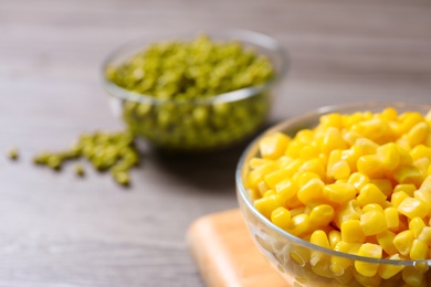 Photo of Glass bowl of canned sweet corn on wooden table, closeup. Space for text