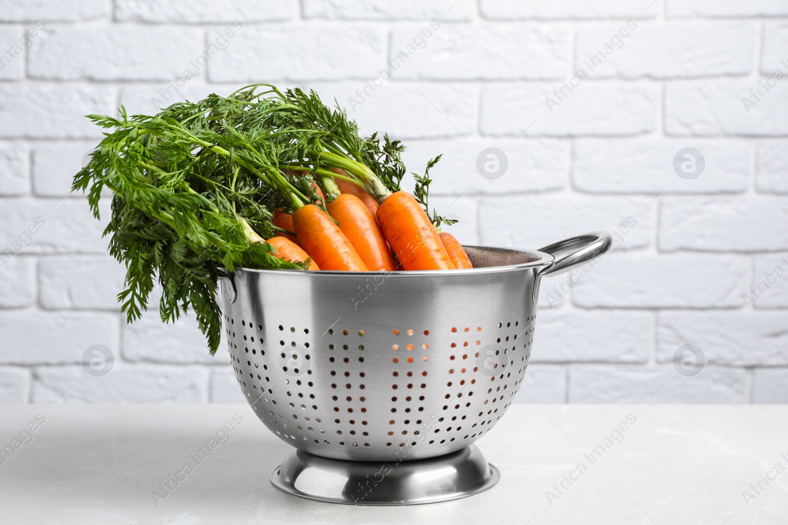 Photo of Colander with fresh ripe carrots on marble table