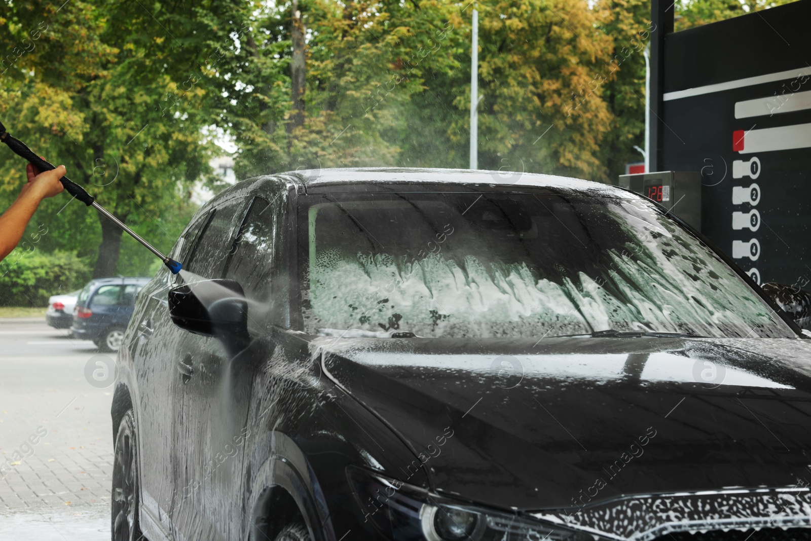 Photo of Man washing auto with high pressure water jet at car wash, closeup