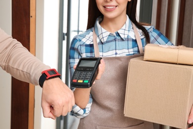 Photo of Young man with smartwatch using terminal for delivery payment indoors, closeup
