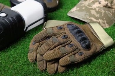 Photo of Tactical gloves, camouflage cap and camping lantern on green grass, closeup. Military training equipment