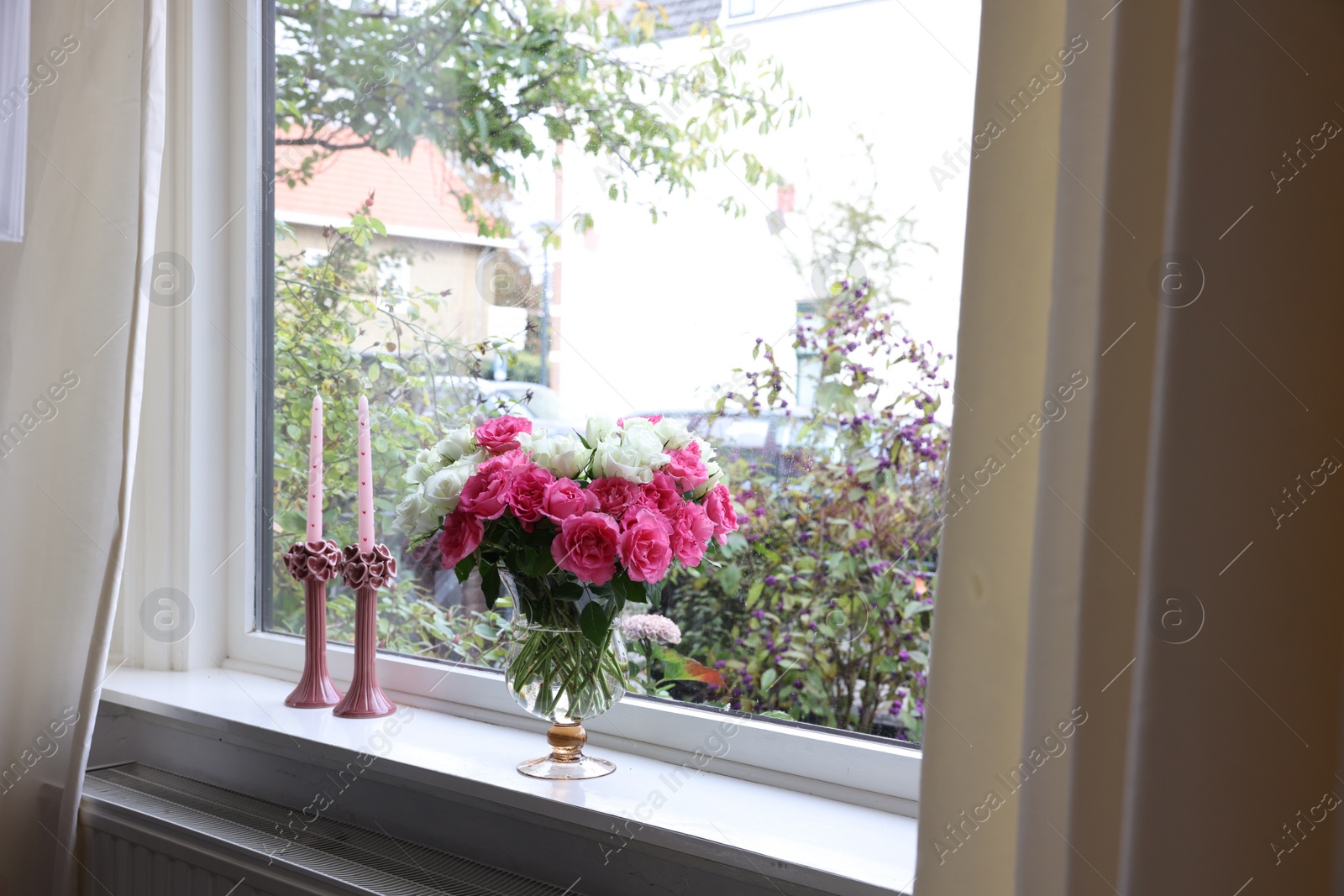 Photo of Vase with beautiful bouquet of roses and candles on windowsill indoors