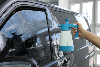 Photo of Worker spraying water onto tinted car window  in workshop, closeup