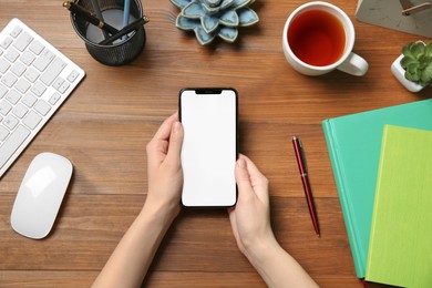 Woman with smartphone at wooden table, top view