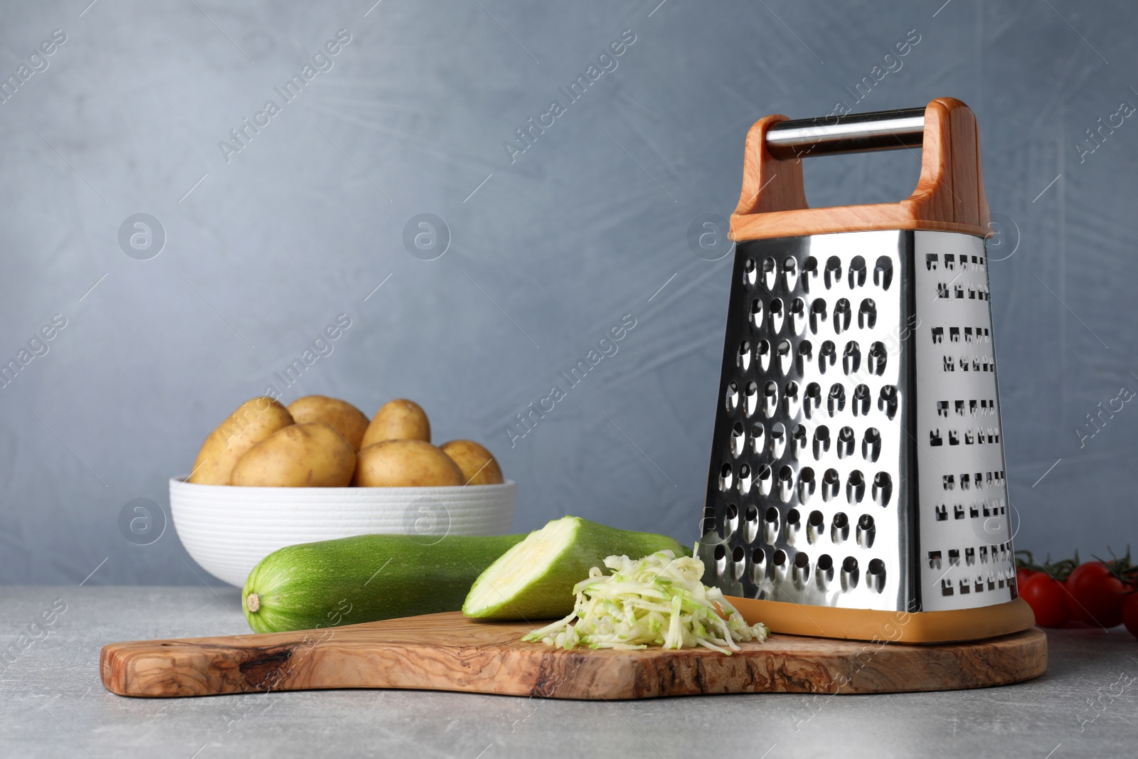 Photo of Grater, fresh zucchinis and potatoes on grey table. Space for text