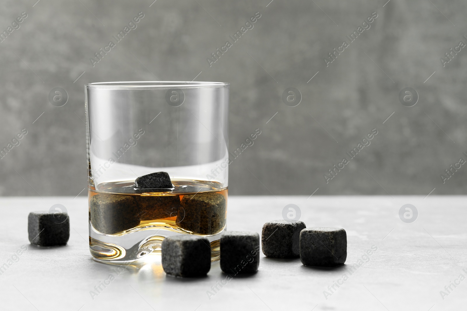 Photo of Whiskey stones and drink in glass on light table, closeup. Space for text