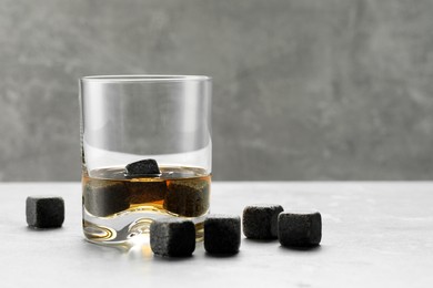 Whiskey stones and drink in glass on light table, closeup. Space for text