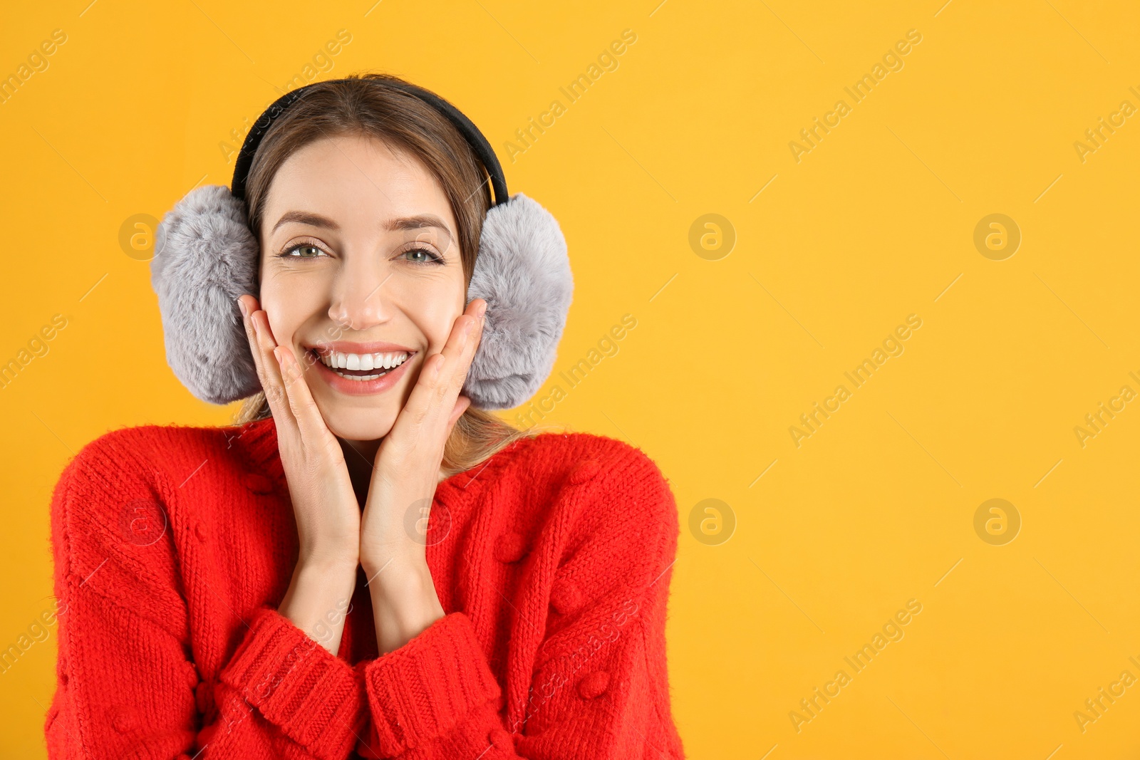 Photo of Happy woman wearing warm earmuffs on yellow background, space for text