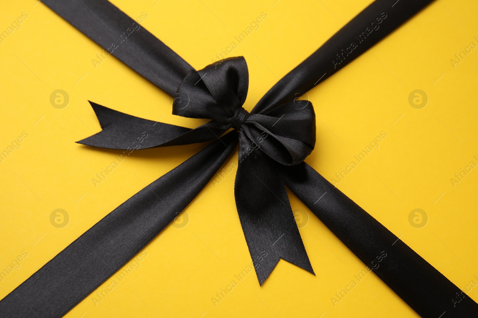 Photo of Black satin ribbon with bow on yellow background