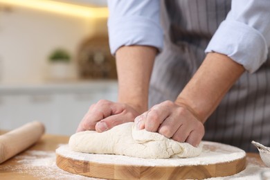 Photo of Making bread. Man kneading dough at wooden table in kitchen, closeup