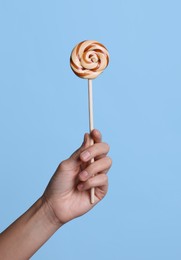 Photo of Woman holding bright tasty lollipop on light blue background, closeup