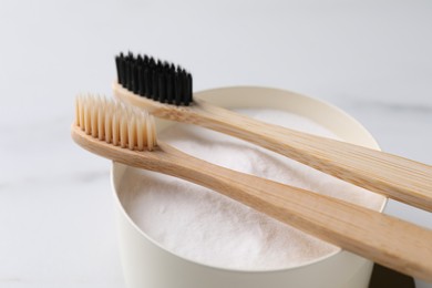 Bamboo toothbrushes and bowl of baking soda on white marble table, closeup