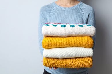 Photo of Woman holding pile of winter sweaters on grey background, closeup view. Space for text