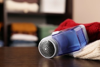 Photo of Modern fabric shaver and knitted clothes on wooden table indoors, closeup. Space for text