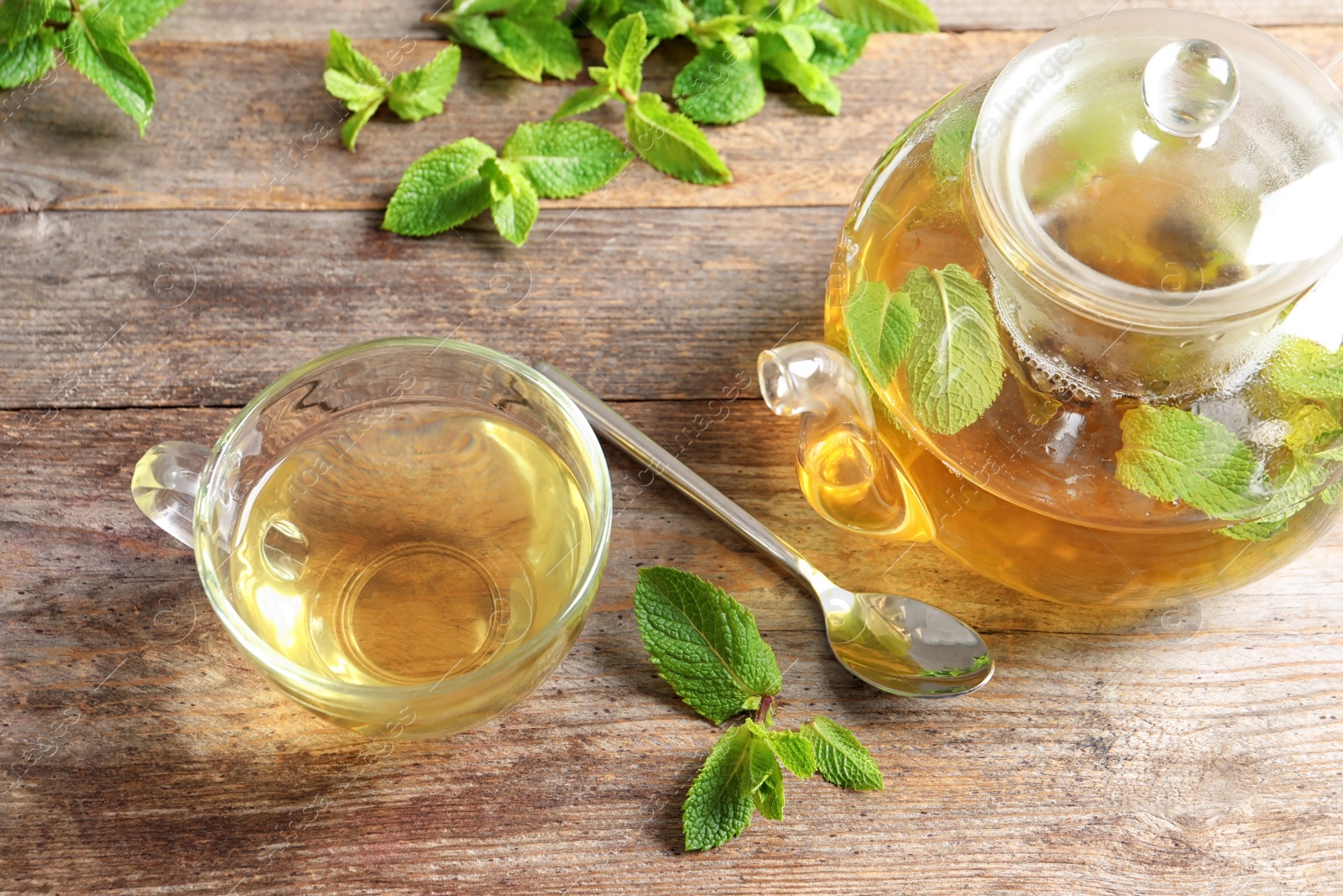 Photo of Cup and teapot with hot aromatic mint tea on wooden table