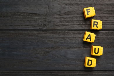 Photo of Word Fraud of yellow cubes with letters on black wooden background, flat lay. Space for text