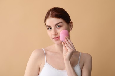 Photo of Washing face. Young woman with cleansing brush on beige background