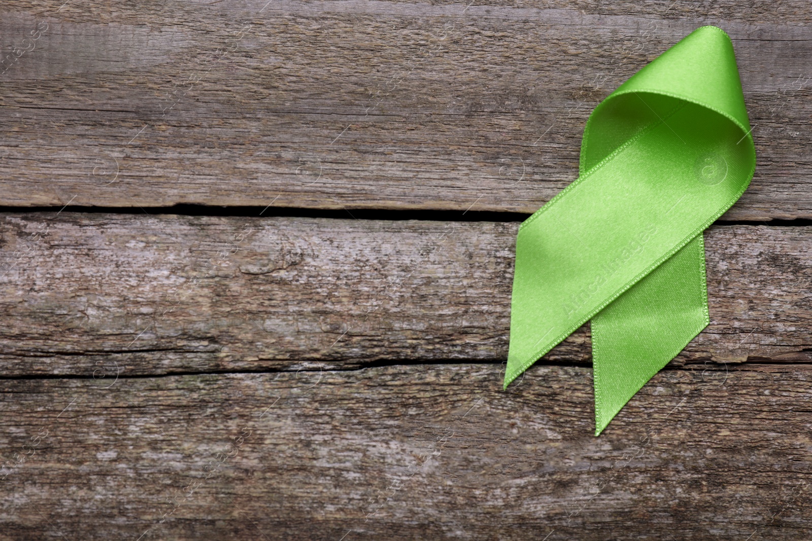 Photo of World Mental Health Day. Green ribbon on wooden background, top view with space for text